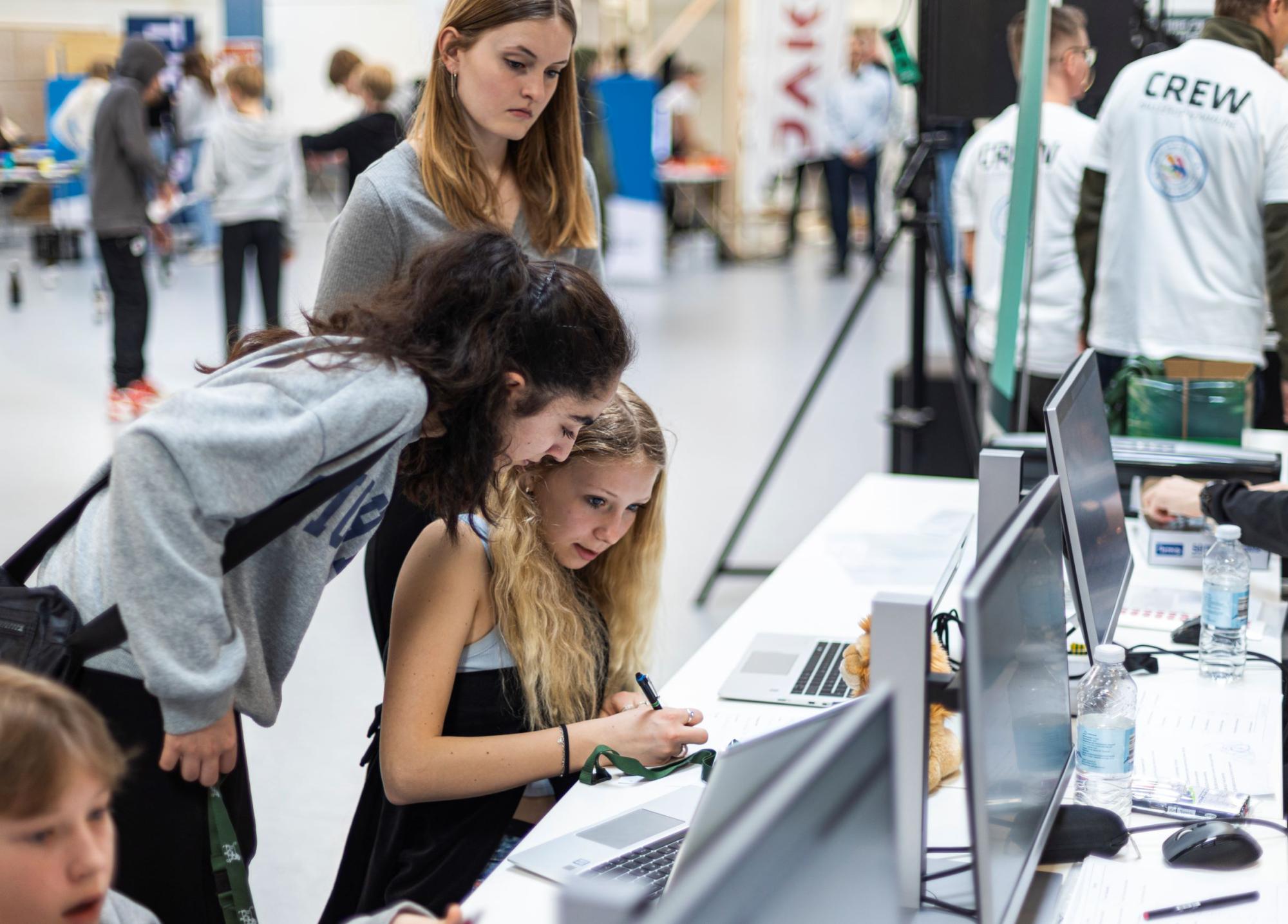 Tre piger kigger på en pc og skriver på papir