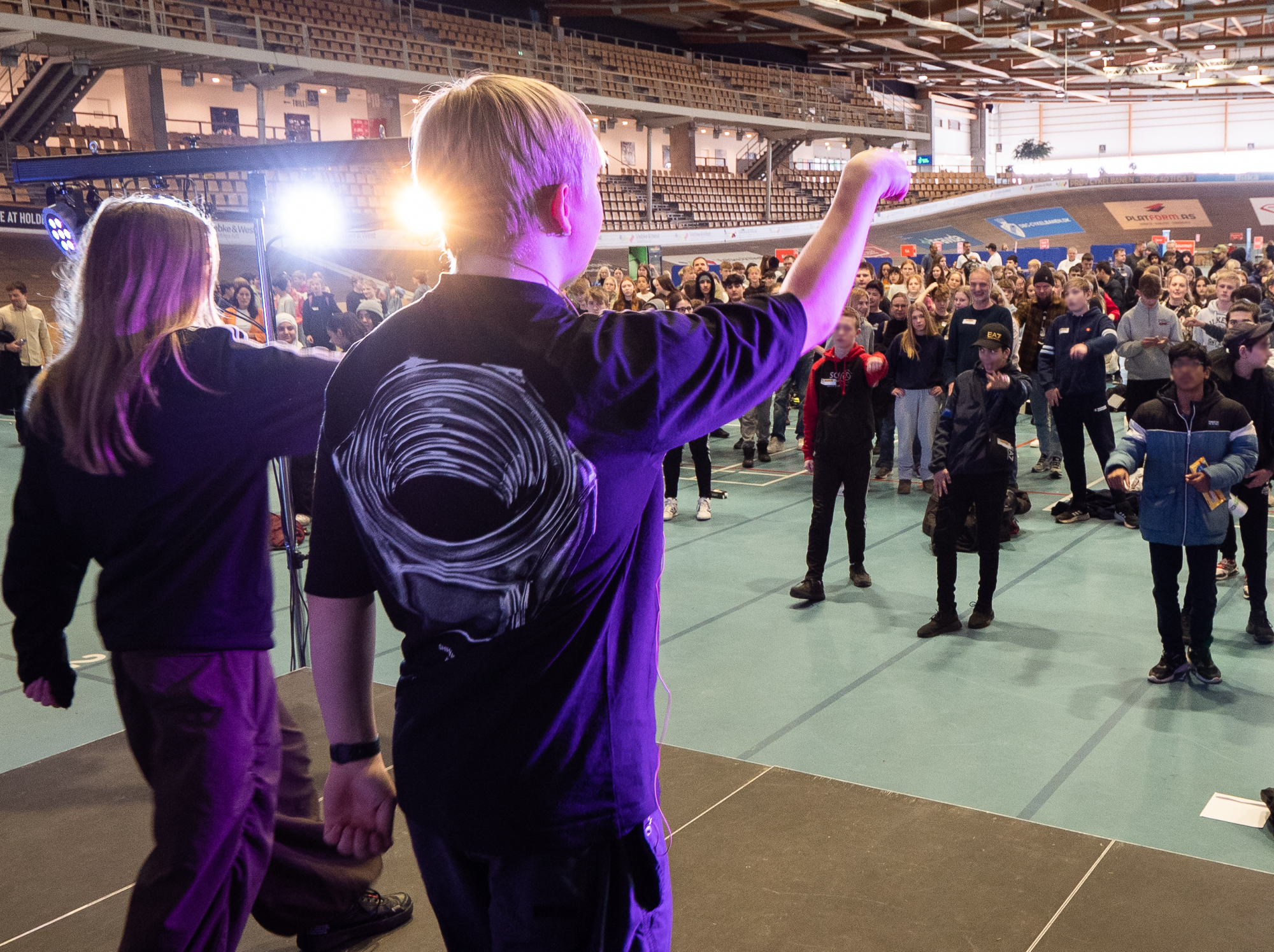 To elever fra 9. klasse står på scenen og danser Mini Skills Ballerup-dansen med 6. klasserne, som står foran scenen.