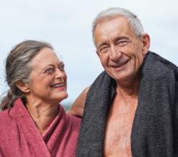 En ældre kvinde i badekåbe kigger på en ældre mand i svømmebukser og håndklæde