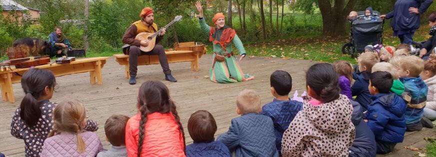 Børn fra en daginstitution kigger på to gøglere, der optræder på dansepladsen på Ballerup Museum
