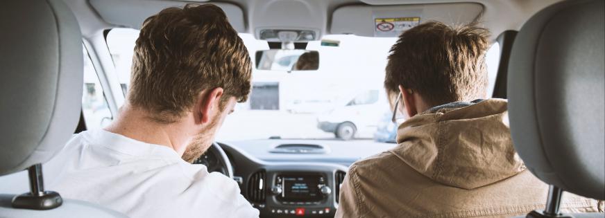 To mænd sidder på forsæderne af en bil og kigger ud af vinduet