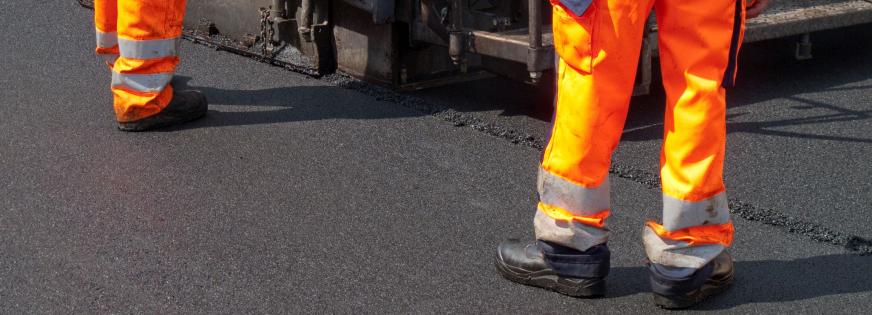 Asfaltmaskine lægger asfalt og to vejfolk arbejder
